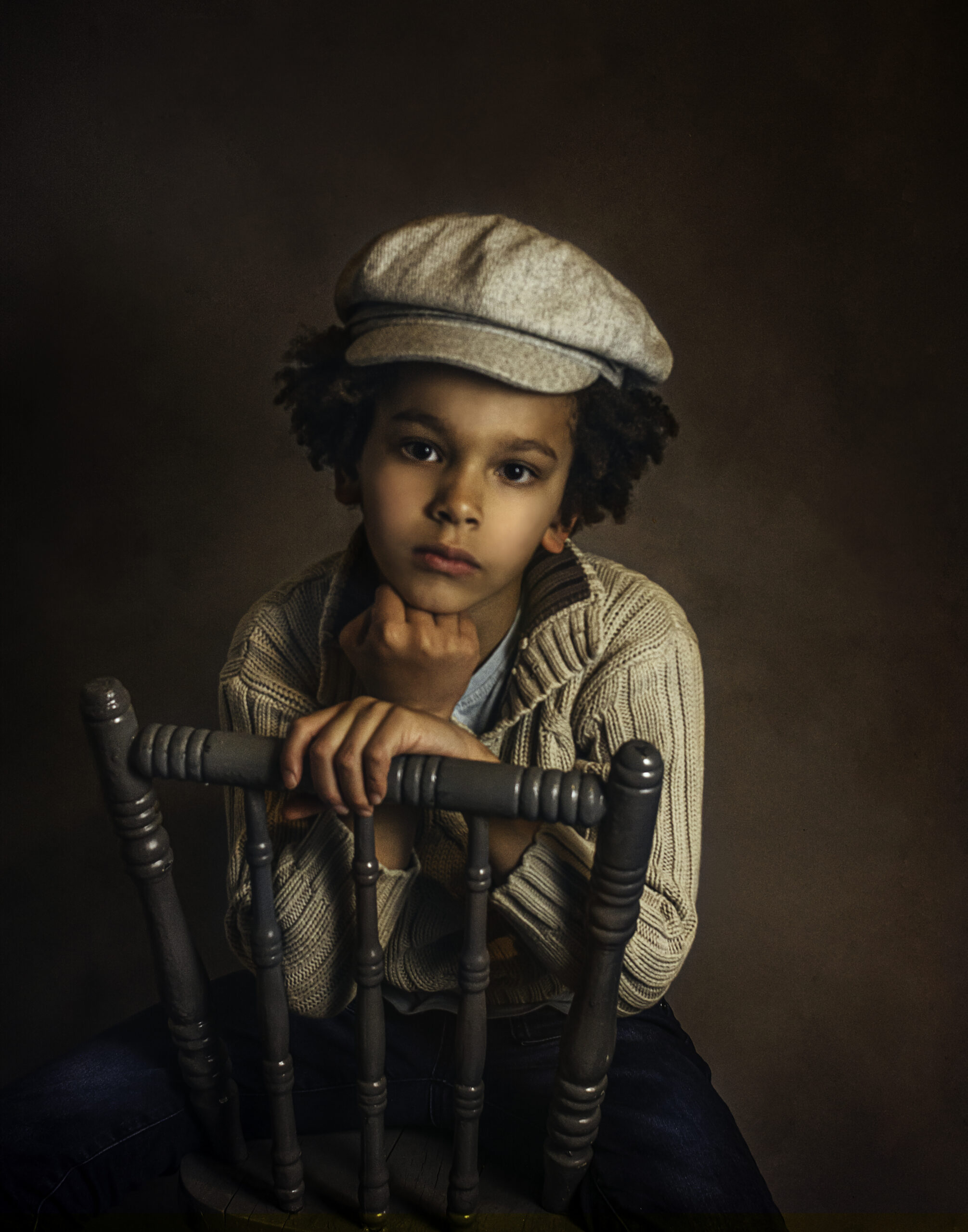 childrens photography child with hat, resting on chair dark curly hair pose